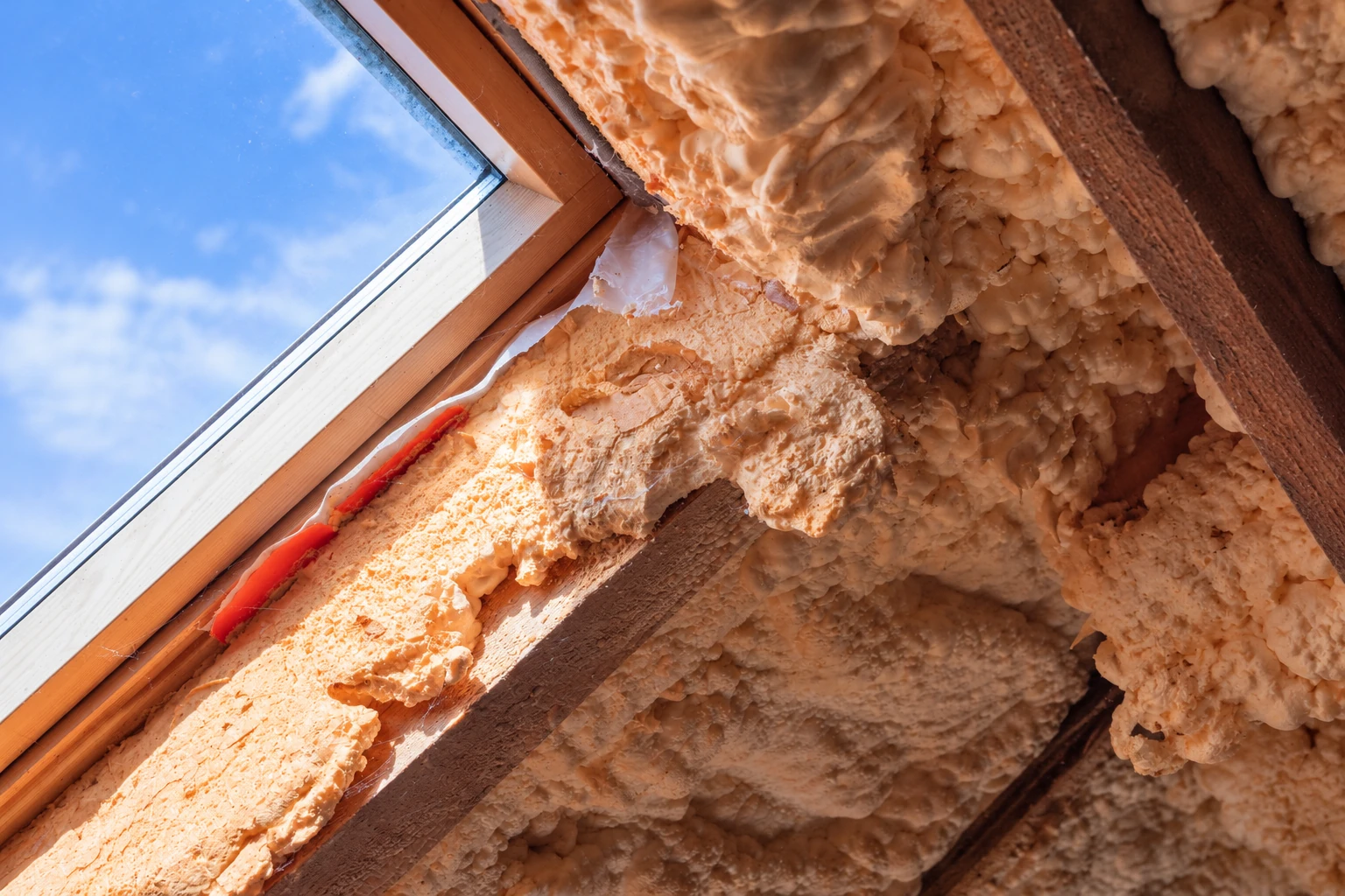 Orange closed-cell foam insulation fills the wooden framing around a sloped roof window.