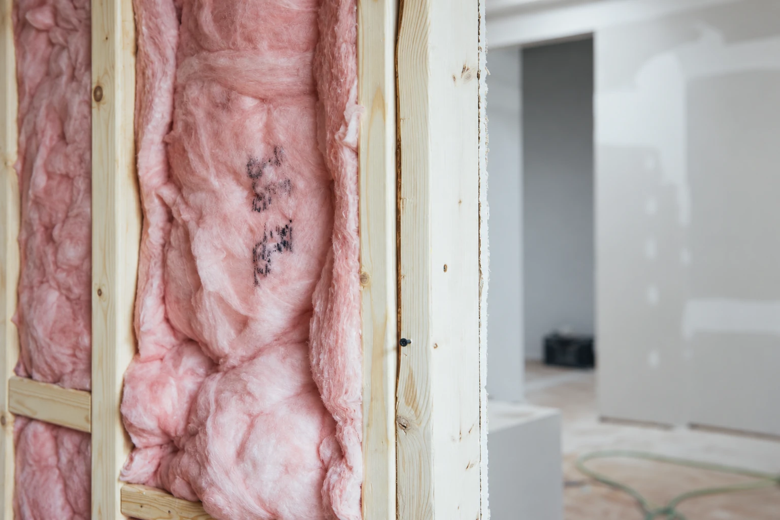 Pink fiberglass insulation fills the wooden studs of an unfinished interior wall.